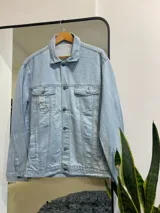 Campera de jean celeste con cuello clásico, cierre con botones metálicos y bolsillos con solapa en el pecho.