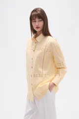 Camisa de algodón blanca, de corte ancho, con botones de madera y detalles de encaje calado en el frente, mangas y ruedo. Tiene cuello camisero y manga larga.