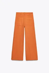 Pantalón de jean color naranja, de tiro alto y pierna ancha. Confeccionado en hilatura con mezcla de algodón. Presenta trabillas en la cintura, bolsillos de plastrón en la espalda y costura marcada en el delantero. Cierre frontal con cremallera, botón y gancho metálico.
