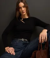 Blusa negra de punto acanalado, con mangas largas, cuello redondo con detalle metálico dorado y abertura asimétrica en el hombro.