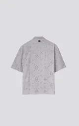 Camisa de manga corta color gris claro con cuello camisero y botones frontales. La tela presenta un bordado tipo broderie con motivos florales y geométricos.