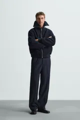 Pantalón de vestir negro, corte recto (straight fit), con cierre frontal de botón y cremallera. Presenta bolsillos delanteros, bolsillos traseros de vivo y un bolsillo de vivo adicional en la pernera.