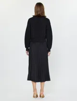 Conjunto de buzo y vestido negro marca Current Air. El vestido es de satén con escote en V y falda plisada. El buzo es de tejido calado, liviano y delicado.