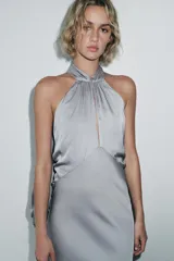 Vestido midi de tejido satinado color gris, con cuello halter, hombros descubiertos, abertura en el pecho, tirantes finos cruzados en la espalda y capa combinada a tono.