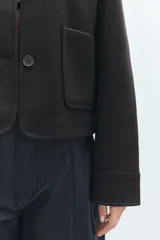 Chaqueta corta negra de cuello solapa y manga larga con puños. Tiene bolsillos de parche en el frente y cierre frontal con botones.