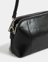 Bandolera negra de cuerina con doble compartimento con cierre y charm lateral. Tiene correa regulable y desmontable.