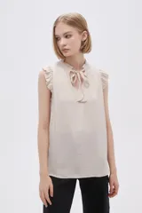 Blusa sin mangas color crudo con cuello con lazo y volados en los hombros.