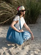 Bolso tote de denim color celeste con asas de hombro y logo bordado en color naranja.