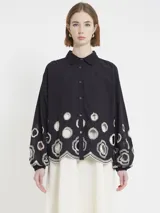 Camisa negra amplia con botones en el frente, mangas abullonadas sobre el puño y apliques de macramé en la parte baja, tanto en el frente como en la espalda y las mangas.