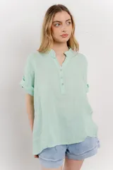 Blusa blanca de lino con escote en V abotonado y mangas cortas arremangadas.