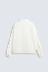 Camisa blanca de corte relajado confeccionada en tejido de algodón y lino. Tiene cuello bowling, manga larga con puños abotonados, jaretas en el delantero, bolsillos de parche en pecho y cadera, bajo con aberturas laterales y cierre frontal con botones.