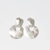 Aros colgantes plateados con forma circular y textura labrada.