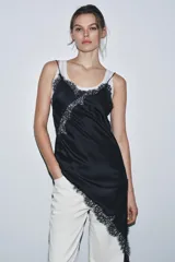 Vestido satinado negro con escote pico y tirantes finos. Presenta aplicación de encaje en el escote y en el bajo asimétrico, que incluye un tajo o caída pronunciada.