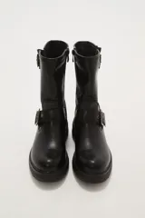 Bota corta de estilo motociclista color negro, con caña media y suela track gruesa. Presenta dos correas ajustables con hebillas metálicas plateadas alrededor del tobillo y la caña.