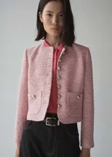 Chaqueta de tweed rosa con cuello redondo, cierre frontal con botones plateados, dos bolsillos de parche delanteros, corte entallado, forro interior y mangas largas.