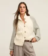 Cardigan de punto color crema con diseño trenzado en el frente, cuello alto, cierre abotonado y mangas largas grises.