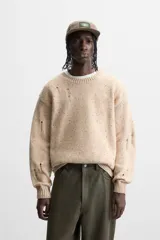 Sweater color beige con detalles de roturas y agujeros.