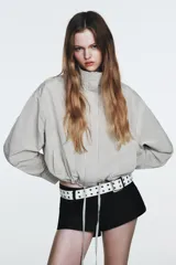 Chaqueta corta de nylon con cuello alto, manga larga y bajo ajustable con cordones. Presenta un estampado de cuadros pequeños en tonos claros.