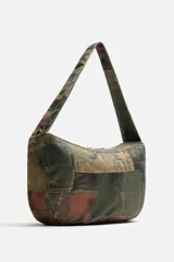 Bolso de hombro tipo bandolera con estampado de parches de denim en tonos verdes, marrones y azules. Tiene un compartimento principal con cierre de cremallera, un bolsillo interior con cremallera y un bolsillo trasero con cremallera. El asa de hombro es ajustable.