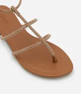 Sandalias planas tipo gladiadoras color tostado, con tiras finas con strass, punta redonda y cierre con hebilla en el tobillo.