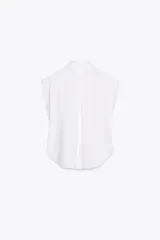 Camisa blanca de popelín con cuello solapa y sisa. Presenta pinzas delanteras y cierre frontal con botones ocultos por solapa.