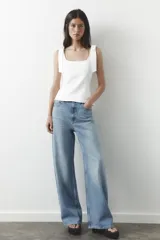 Top blanco de tejido elástico con escote cuadrado y tirantes anchos con lazos decorativos.