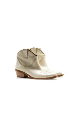 Botas de caña baja color crema, estilo texanas, con bordados a tono en la puntera y caña. Cuentan con un tacón bajo y punta alargada redondeada con suela cuadrada de terminación lisa que sobresale levemente.