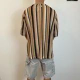 Remera tejida de punto con rayas verticales en tonos beige, marrón y negro, de corte oversize y mangas cortas.