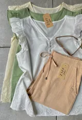 Blusa beige con detalles de volantes y cierre frontal, confeccionada en tejido ligero.