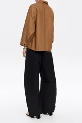 Chaqueta corta color marrón de corte recto, confeccionada en mezcla de lino y algodón. Tiene cuello camisero, botonadura frontal oculta, manga larga con pliegues en los codos, bolsillos plastrón en delantero y pecho, y pespunte a contraste en bolsillos, bajo y puños.