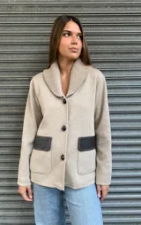 Campera de punto color beige con cuello tipo chal y cierre con tres botones. Tiene dos bolsillos frontales con solapa de cuero marrón.