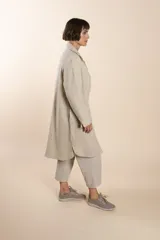 Camisa larga color crema con rayas verticales finas en gris, con botones dorados y bolsillo plaque en la delantera.