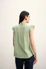 Camisa color amarillo pálido con cuello mao, sin mangas, con volados en los hombros y en el frente.