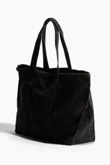 Bolso shopper grande de denim negro con efecto lavado. Tiene dos asas cortas, un bolsillo exterior abierto y un compartimento interior pequeño.