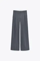 Pantalón gris de tiro alto con trabillas, doble pliegue, bolsillos laterales y de vivo en espalda, pernera ancha y cierre frontal con cremallera y gancho metálico.