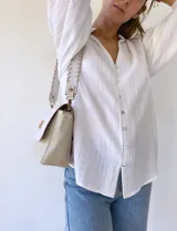Bandolera color crudo con solapa de gamuza y cuerpo de cuero sintético texturizado. Tiene correa corta de cuero con tientos y forro de tela con bolsillo interno.