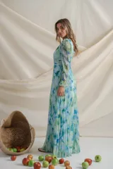 Vestido largo de gasa plisada con estampado floral en tonos celeste, verde y azul. Tiene escote cruzado con detalle de alforzas, mangas largas con abertura y falda plisada. Ideal para eventos de día.