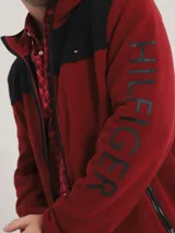 Campera con capucha Tommy Hilfiger, color rojo y negro, con cierre de cremallera, bolsillos laterales con cierre y logo de la marca bordado en el pecho.