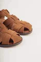 Sandalias bajas de cuero marrón con tiras entrecruzadas y hebilla dorada.