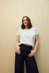 Remera de manga corta color gris claro, confeccionada en algodón con textura liviana y suave al tacto. Presenta costuras decorativas en los laterales y mangas con pequeño doblez.