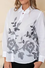 Camisa blanca de algodón con bordado floral en hilo negro en el frente. Camisa de corte clásico, con cuello abotonado, mangas largas con puños abotonados y cierre frontal con botones.