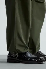 Pantalón verde militar de corte relaxed fit confeccionado en tejido técnico ligero. Cuenta con cintura elástica ajustable con cordón interior, bolsillos frontales y traseros con solapa, pliegues en las rodillas y bajo ajustable con elástico.