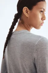 Cárdigan gris de punto suave con cuello redondo y botones metálicos dorados en el frente. Tiene remate acanalado en cuello, puños y bajo.