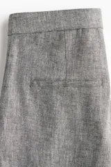 Pantalón de vestir gris claro, de tiro alto, con bolsillos laterales y traseros. Piernas amplias con pliegues delanteros y traseros. Confeccionado en tejido liviano de mezcla de lino y viscosa.