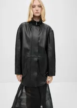 Abrigo negro de cuero con cuello alto, cierre frontal con cremallera y bolsillos laterales. Diseño oversize y largo.