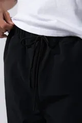 Pantalón de jogging negro de taslan con corte holgado, cintura elástica con cordón ajustable, bolsillos laterales y puños elásticos. Presenta una franja blanca a lo largo de la pierna y logo bordado en blanco.