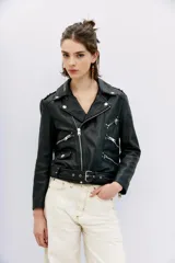 Campera negra de cuero ovino, estilo rocker, con cinturón, charreteras y solapas. Tiene cierres y detalles metálicos en frente y espalda.