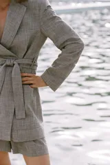 Blazer marrón claro con estampado a cuadros, cuello solapa, manga larga con hombreras, bolsillos delanteros y cierre cruzado con cinturón del mismo tejido.