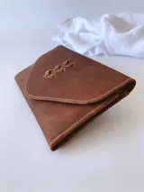 Billetera de cuero marrón con sistema de cierre con broche, monedero externo y detalle de hojas grabadas en la solapa.