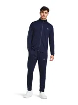 Conjunto deportivo Under Armour, compuesto por campera con cierre y pantalón largo. Ambos de color azul marino con detalles en gris. La campera tiene cuello alto, cierre frontal completo y logo de la marca en el pecho. El pantalón tiene cintura elástica con cordón ajustable y logo de la marca en la pierna.